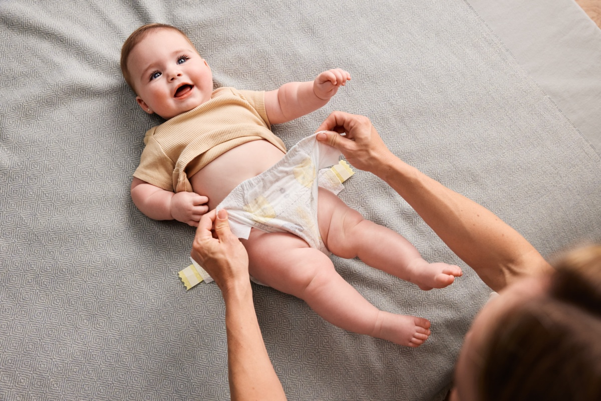 Parent en train de changer la couche d'un bébé allongé sur un tapis