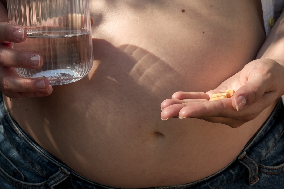 Femme enceinte tenant un verre d'eau et des compléments alimentaires dans sa main