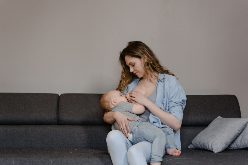 Maman allaitant son bébé assise sur un canapé gris dans son salon