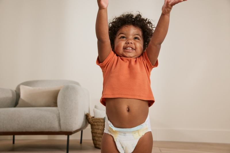 Bébé debout en couche les bras levés dans un salon