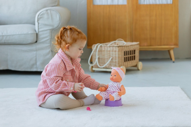 Petite fille jouant avec une poupée assise sur un pot pour enfant