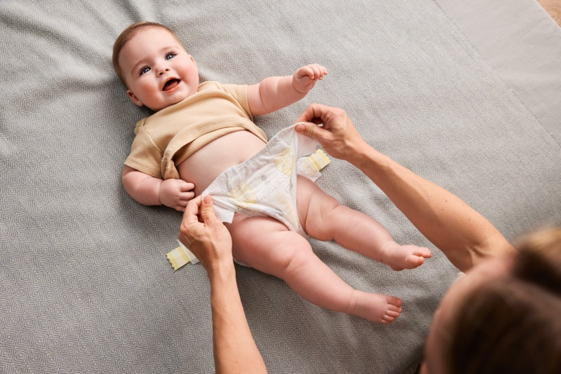 Parent en train de changer la couche d'un bébé allongé sur un tapis