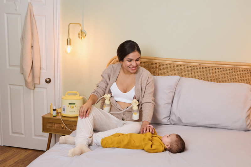 Maman utilisant le tire-lait électrique Medela Symphony sur son lit, à côté de son bébé