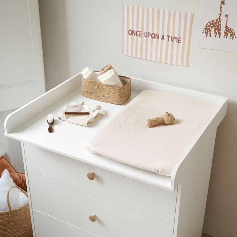 Commode blanche avec plan à langer et panier contenant les affaires de toilette de bébé
