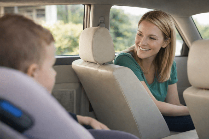 Maman assise à l'avant d'une voiture regardant son enfant installé dans un siège auto à l'arrière