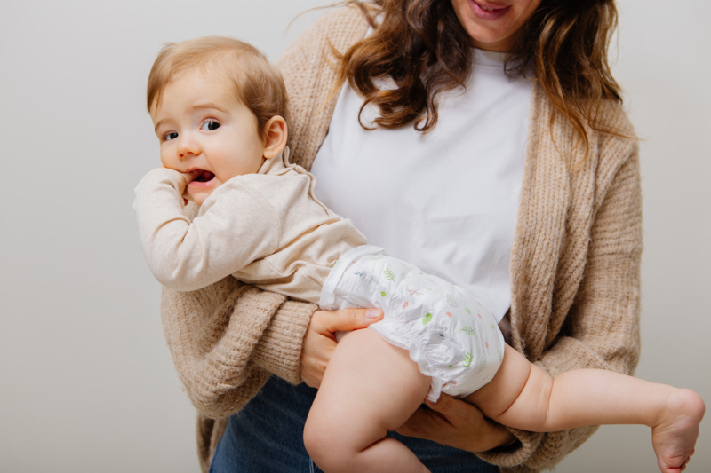 Bébé en couche avec un doigt dans la bouche dans les bras d'un parent