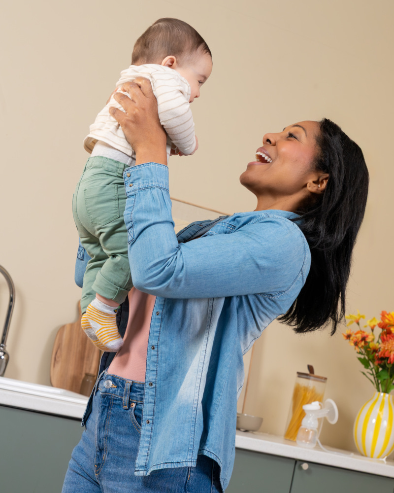 Maman portant son bébé dans les bras dans une cuisine lumineuse, instant de tendresse parent-enfant
